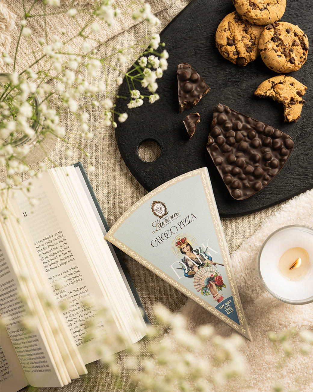 Laurence Pizza Tafelschokolade Zartbitter mit Choco-Balls Packung & Tafel auf einem Brettchen mit Cookies, auf einem Tisch mit Kerze, Buch und Blumen Laurence Pizza Tafelschokolade Zartbitter mit Choco-Balls Packung & Tafel auf einem Brettchen mit Cookies, auf einem Tisch mit Kerze, Buch und Blumen