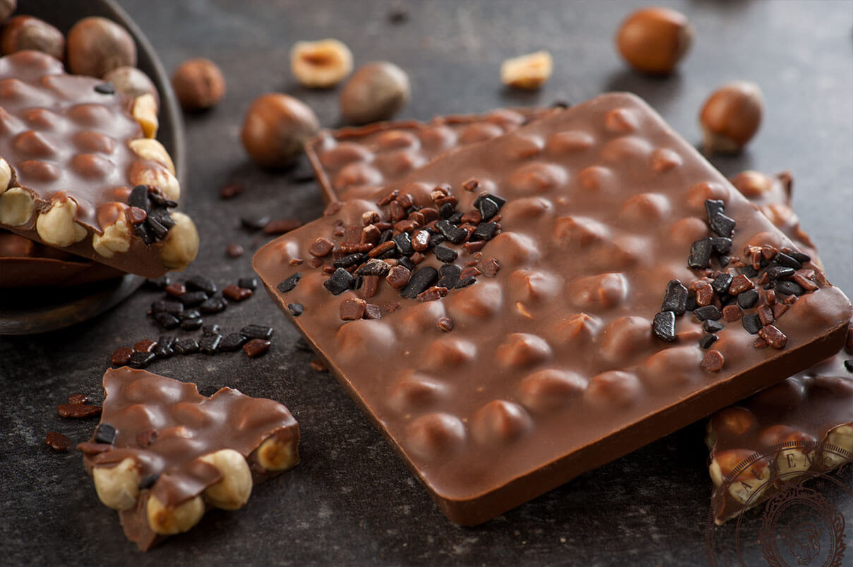 Laurence Tafelschokolade Signature Edition Vollmilchschokolade mit Haselnüssen fein angerichtet auf einer Unterlage Laurence Tafelschokolade Signature Edition Vollmilchschokolade mit Haselnüssen fein angerichtet auf einer Unterlage