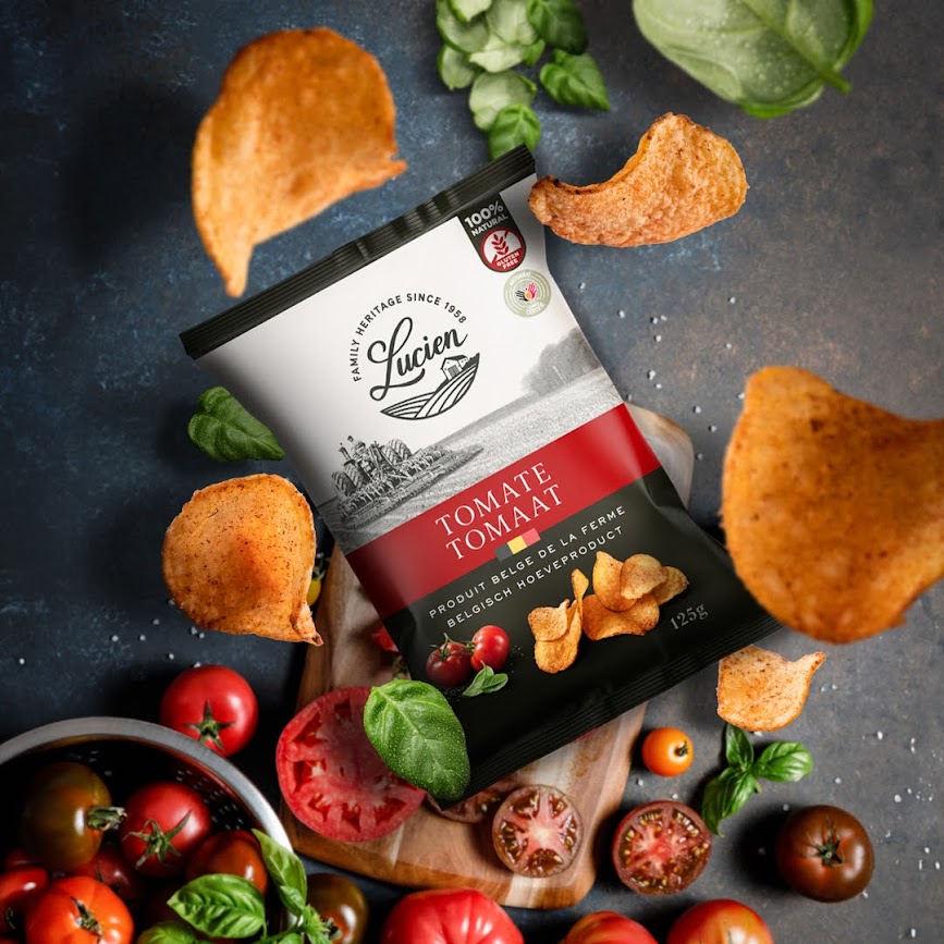 Lucien Chips Tomate Packung liegt auf einem Holzbrettchen, dass auf einer Granitplatte liegt, direkt daneben steht eine Schale mit Tomaten, es liegen auch aufgeschnittene Tomaten und Basilikum daneben, von oben fallen Chips herunter Lucien Chips Tomate Packung liegt auf einem Holzbrettchen, dass auf einer Granitplatte liegt, direkt daneben steht eine Schale mit Tomaten, es liegen auch aufgeschnittene Tomaten und Basilikum daneben, von oben fallen Chips herunter