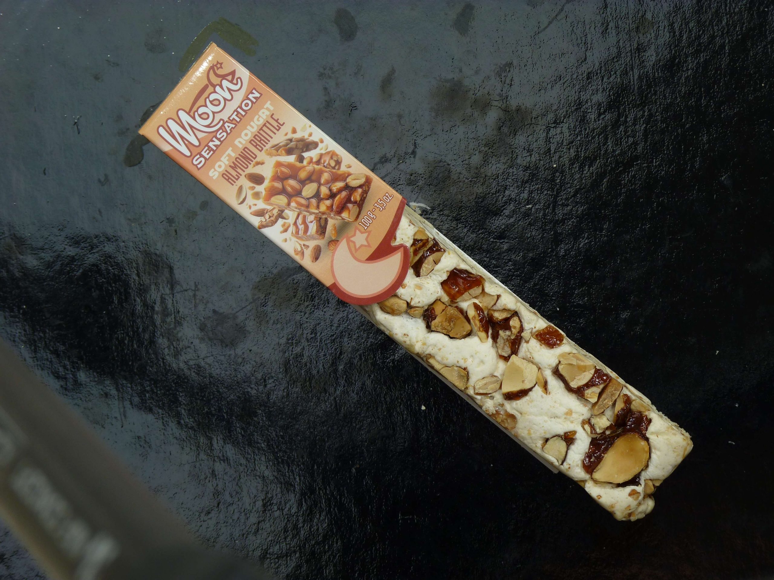 Moon Softnougat Stange Mandelkrokant in der Verpackung auf einem schwarzem Hintergrund Moon Softnougat Stange Mandelkrokant in der Verpackung auf einem schwarzem Hintergrund