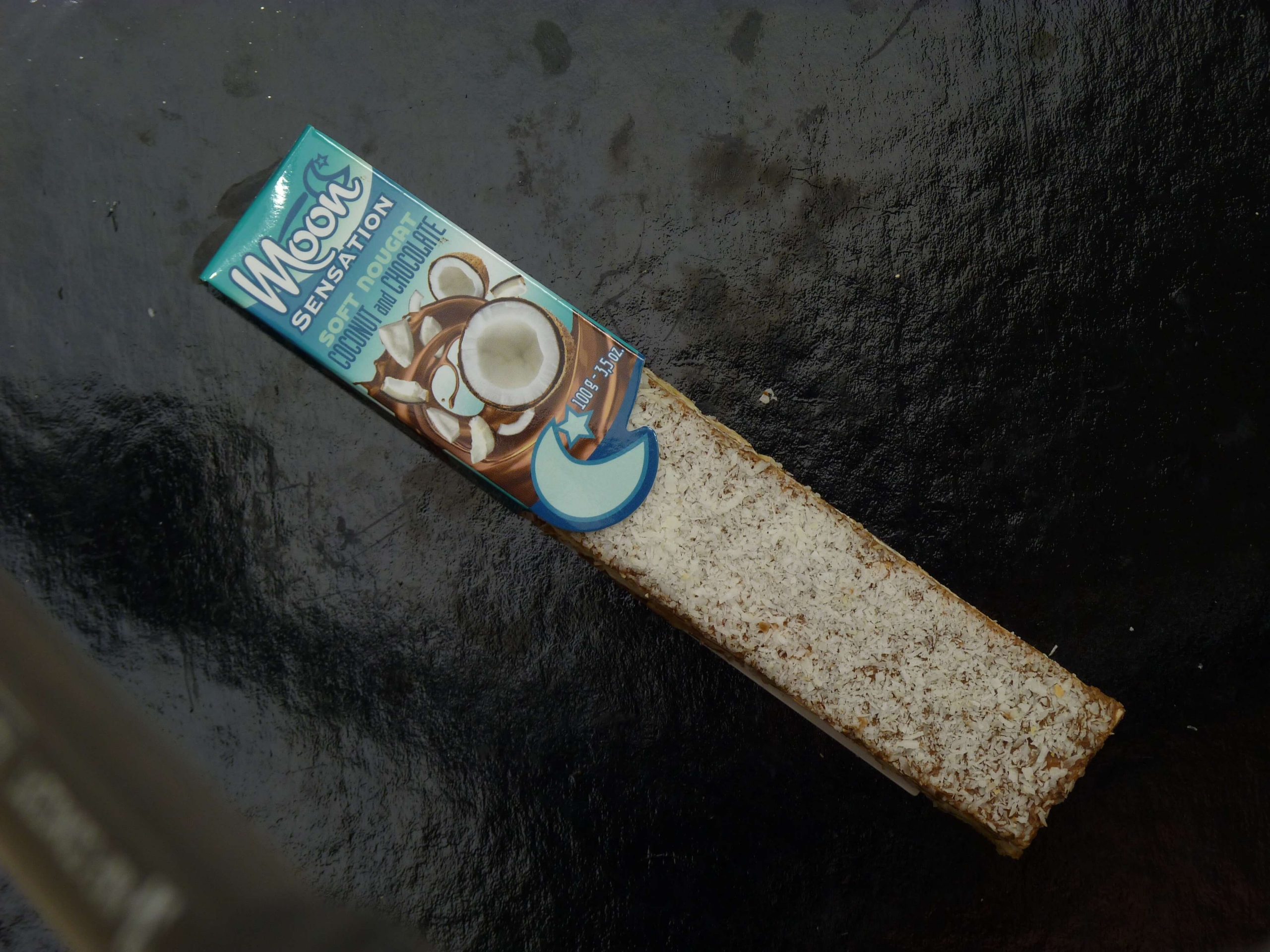 Moon Softnougat Stange Kokosnuss Milchschokolade in der Verpackung auf einem schwarzen Hintergrund Moon Softnougat Stange Kokosnuss Milchschokolade in der Verpackung auf einem schwarzen Hintergrund