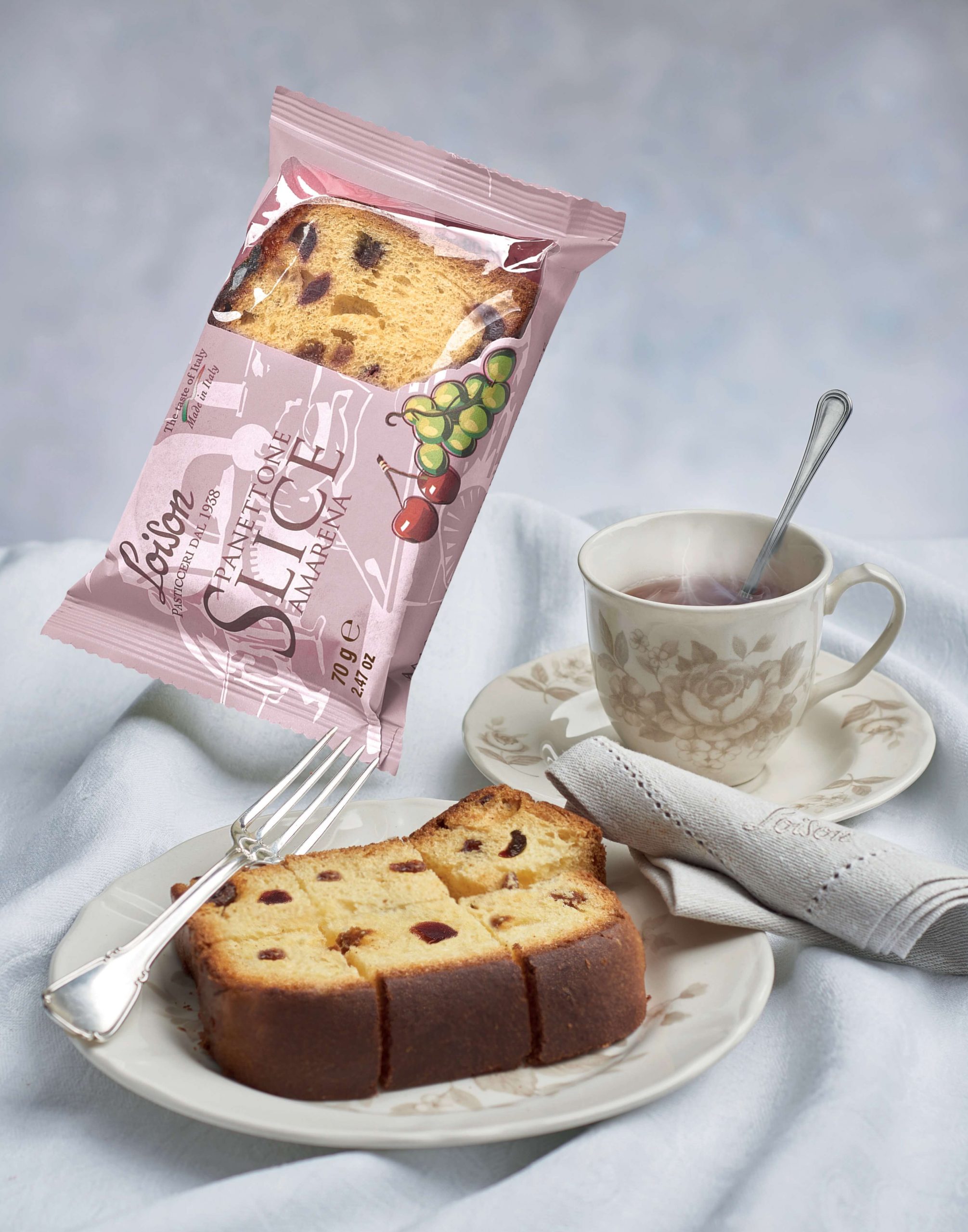 Loison Panettone Amarena Scheibe auf einem Teller auf einem gedeckten Tisch mit Tasse Tee Loison Panettone Amarena Scheibe auf einem Teller auf einem gedeckten Tisch mit Tasse Tee